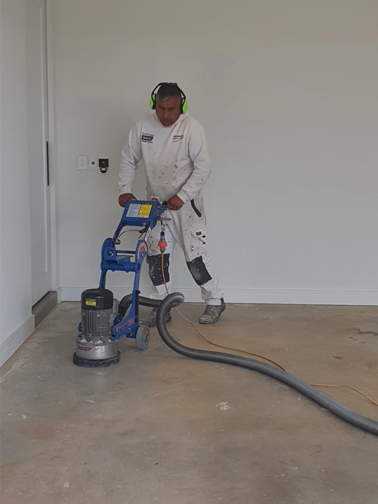 Worker using floor sanding machine in empty room