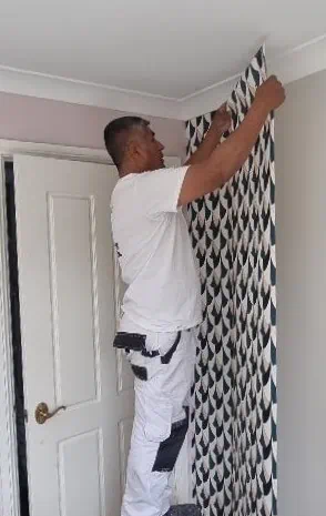 Man hanging wallpaper in room