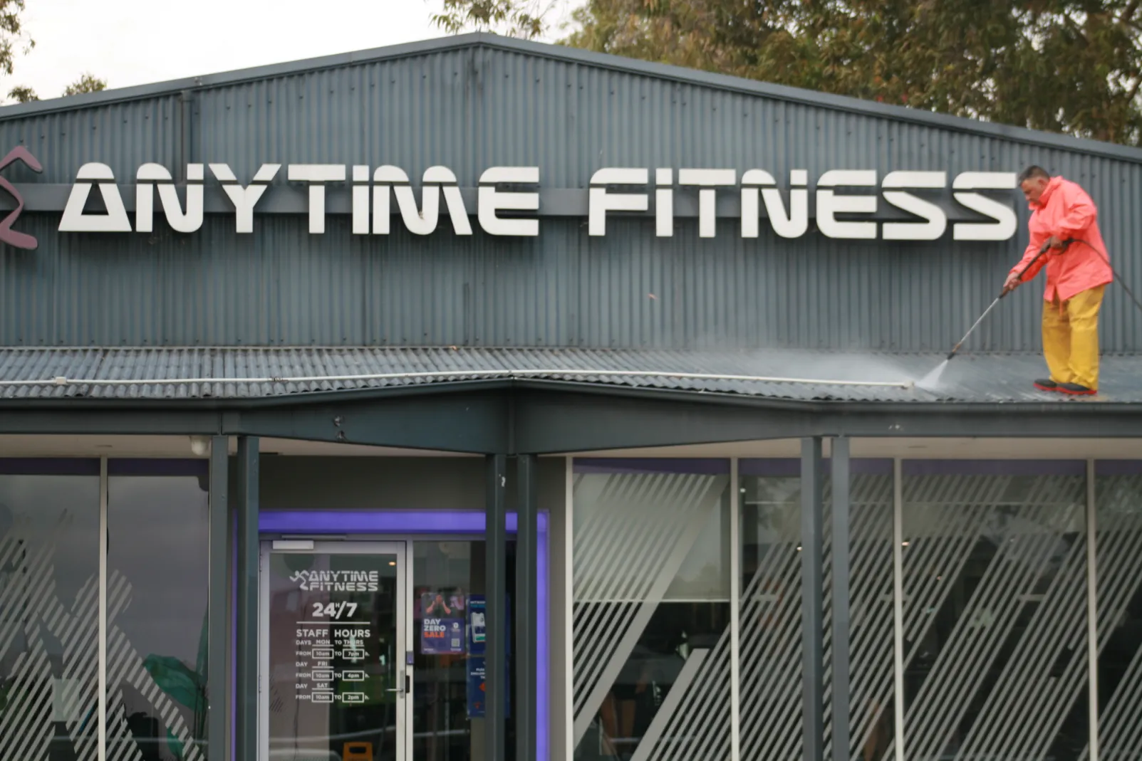 Worker cleaning Anytime Fitness gym roof with hose