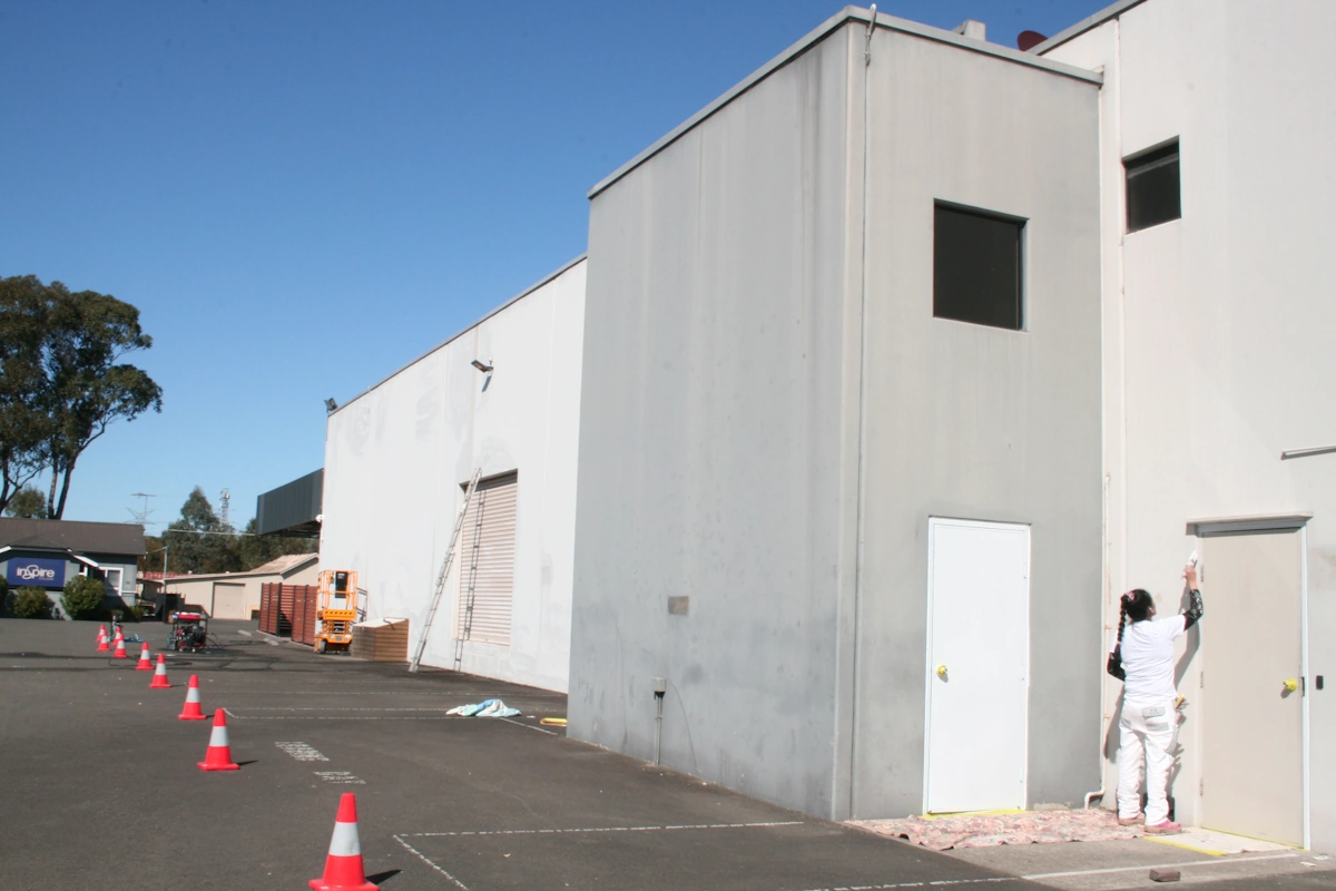 Painter working on white building exterior with traffic cones
