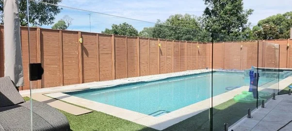 Backyard swimming pool with wooden fence and glass barrier