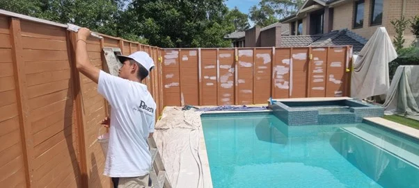 Man painting wooden fence by backyard pool