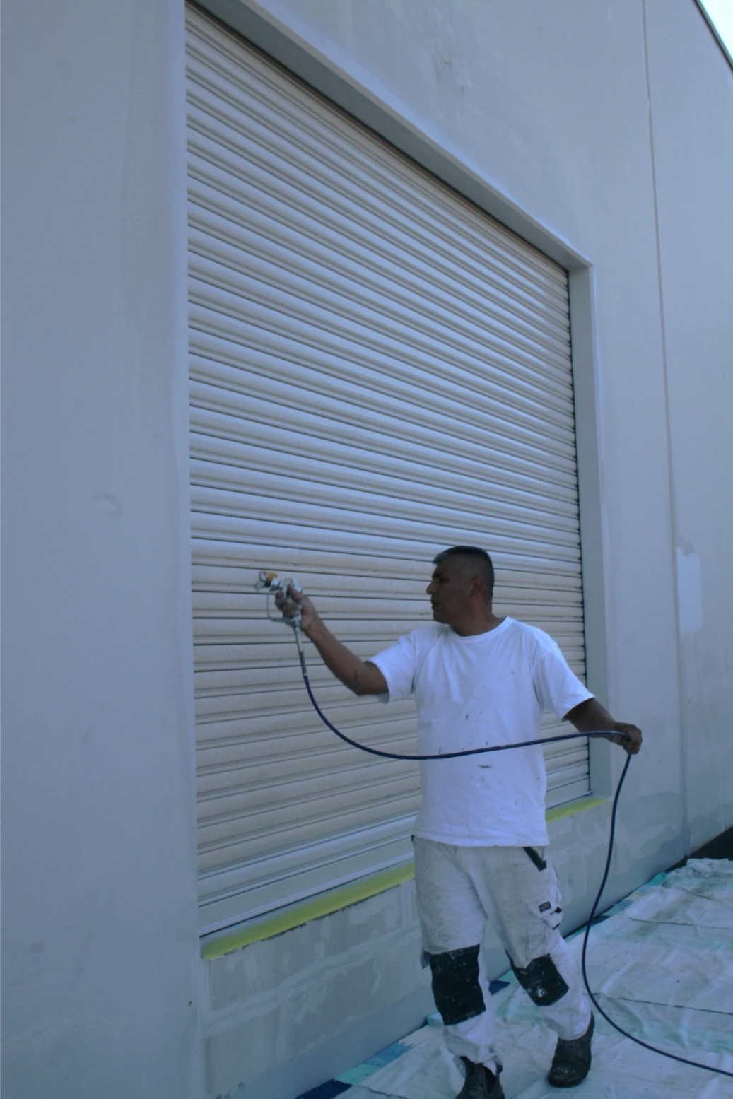 Man painting garage door with spray gun