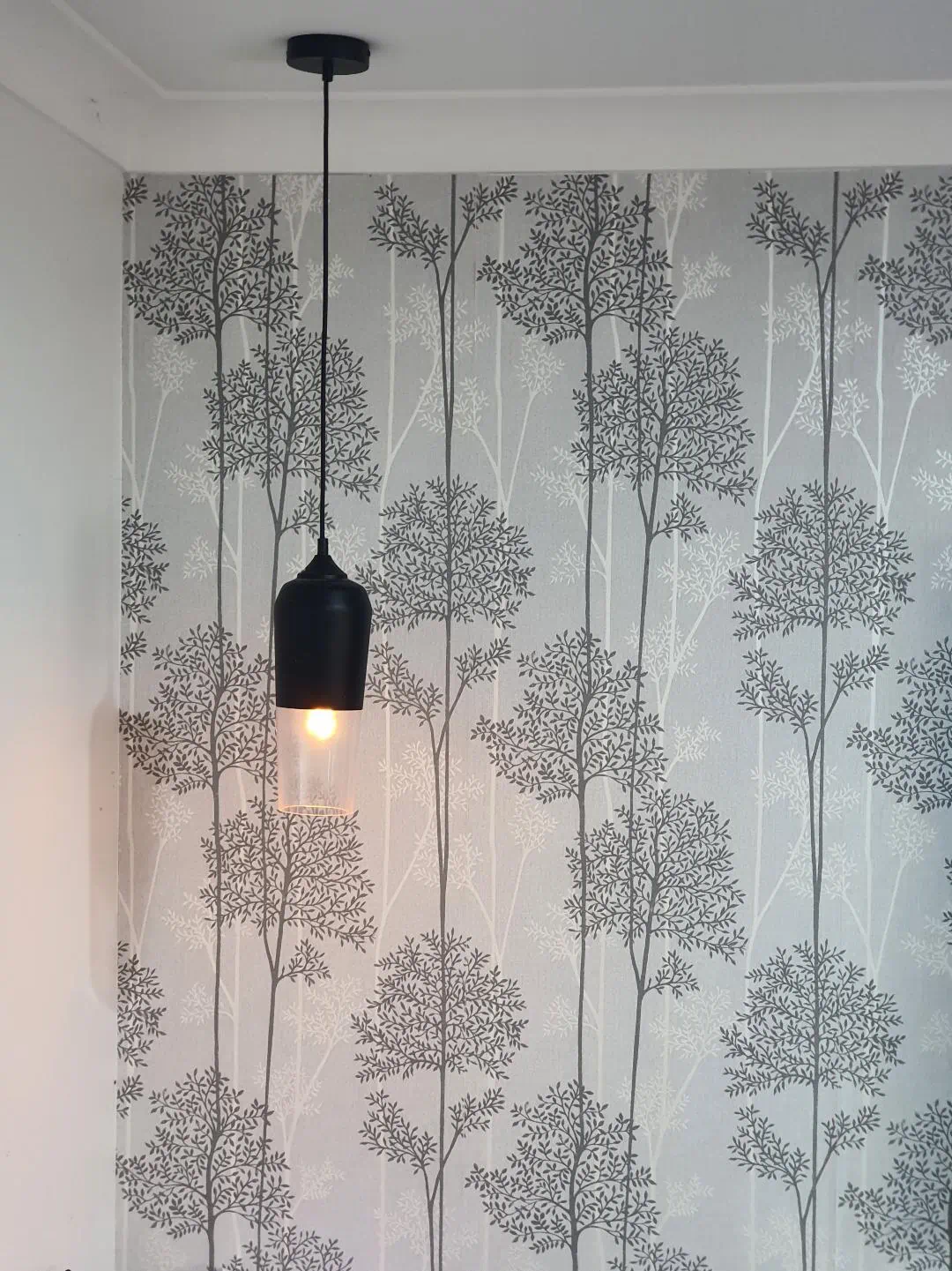 Minimalist pendant light against tree patterned wallpaper